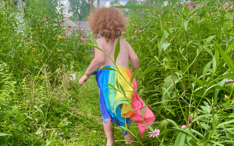 little girl running through a yard with native plants, wearing a rainbow skirt