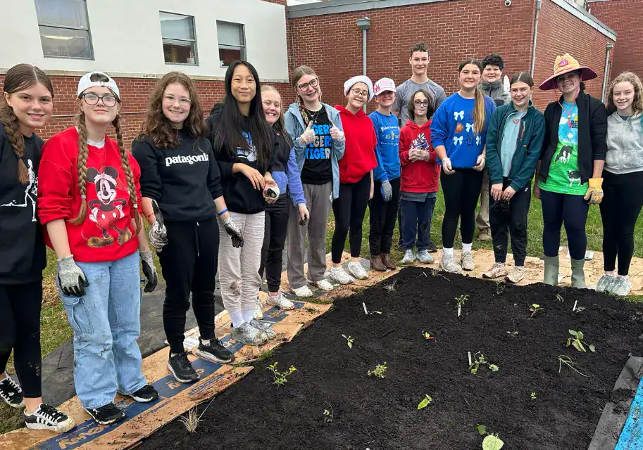 A group of middle-school students and teachers stand smiling behind a newly planted native garden bed at their school.