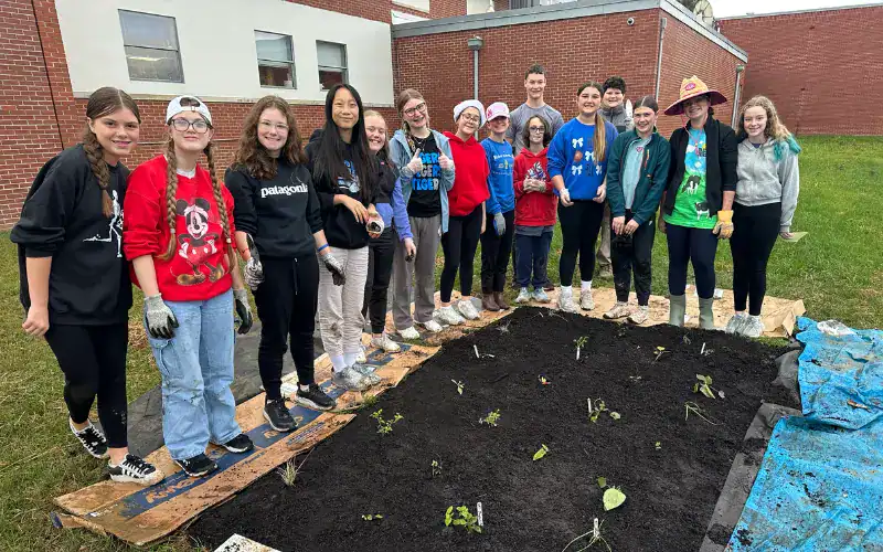 A group of middle-school students and teachers stand smiling behind a newly planted native garden bed at their school.